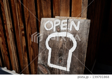 パン屋の開店。白いOPENの文字と食パンのイラスト。木製の看板。 パン屋の開店。白いOPENの文字と食パンのイラスト。木製の看板。 139701868
