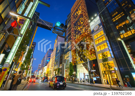 Tokyo, Japan - Oct 14 2024,  A panoramic view of street in Ginza district with cars driving along road with their headlights on, facades of skyscrapers are full of lights and signs of various shops 139702160