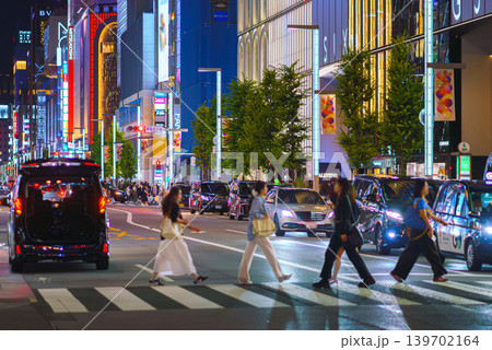 Tokyo, Japan - Oct 14 2024, panoramic view of people crossing road at pedestrian crossing in Ginza district, with many illuminated signage on facades of skyscrapers in background and cars Tokyo, Japan - Oct 14 2024, panoramic view of people crossing road at pedestrian crossing in Ginza district, with many illuminated signage on facades of skyscrapers in background and cars 139702164