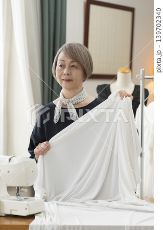 シニア女性のデザイナーがアトリエで洋服を作る シニア女性のデザイナーがアトリエで洋服を作る 139702340