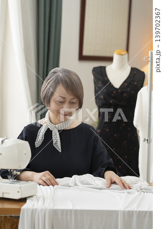 シニア女性のデザイナーがアトリエで洋服を作る シニア女性のデザイナーがアトリエで洋服を作る 139702367
