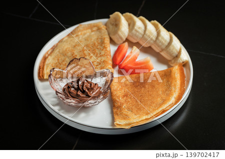 A plate of crepes filled with chocolate spread and topped with banana slices and mint A plate of crepes filled with chocolate spread and topped with banana slices and mint 139702417