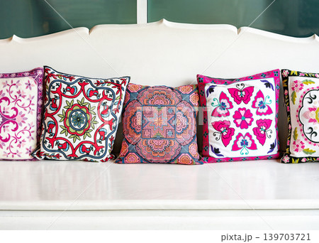 Many square pillow with colorful floral geometric pattern are arranged orderly on the white wooden sofa. 139703721