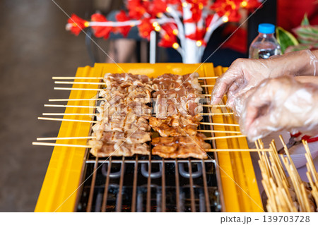 The shot of a cook grill Moo Ping or grilled pork skewers in Thai style on the yellow electric barbeque grill at the restaurant. The shot of a cook grill Moo Ping or grilled pork skewers in Thai style on the yellow electric barbeque grill at the restaurant. 139703728