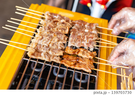 The shot of a cook grill Moo Ping or grilled pork skewers in Thai style on the yellow electric barbeque grill at the restaurant. The shot of a cook grill Moo Ping or grilled pork skewers in Thai style on the yellow electric barbeque grill at the restaurant. 139703730