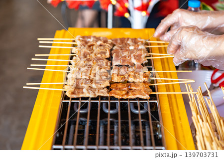 The shot of a cook grill Moo Ping or grilled pork skewers in Thai style on the yellow electric barbeque grill at the restaurant. The shot of a cook grill Moo Ping or grilled pork skewers in Thai style on the yellow electric barbeque grill at the restaurant. 139703731