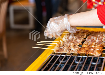 The shot of a cook grill Moo Ping or grilled pork skewers in Thai style on the yellow electric barbeque grill at the restaurant. The shot of a cook grill Moo Ping or grilled pork skewers in Thai style on the yellow electric barbeque grill at the restaurant. 139703732
