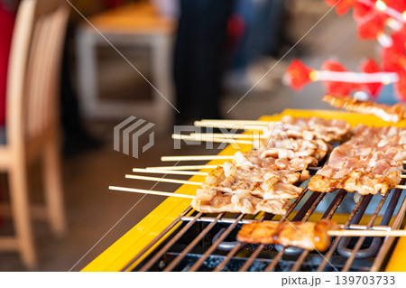 The shot of a cook grill Moo Ping or grilled pork skewers in Thai style on the yellow electric barbeque grill at the restaurant. The shot of a cook grill Moo Ping or grilled pork skewers in Thai style on the yellow electric barbeque grill at the restaurant. 139703733