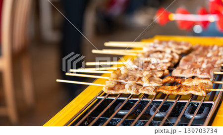 The shot of a cook grill Moo Ping or grilled pork skewers in Thai style on the yellow electric barbeque grill at the restaurant. The shot of a cook grill Moo Ping or grilled pork skewers in Thai style on the yellow electric barbeque grill at the restaurant. 139703734
