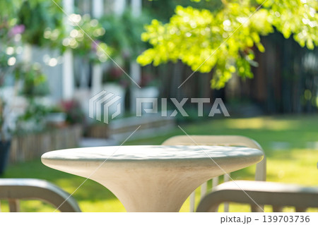 The outdoor furniture set, a white round table with seats, placed in the peaceful and shady garden. Shadow of branches and leaves project on outdoor furniture. The outdoor furniture set, a white round table with seats, placed in the peaceful and shady garden. Shadow of branches and leaves project on outdoor furniture. 139703736