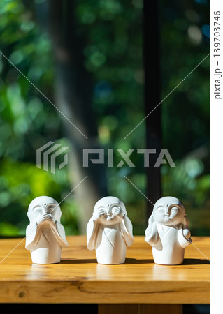 Three white monk figurines inspired by the Three Wise Monkeys philosophy are displayed as minimal zen decoration on a wooden tabletop with peaceful spiritual atmosphere. Three white monk figurines inspired by the Three Wise Monkeys philosophy are displayed as minimal zen decoration on a wooden tabletop with peaceful spiritual atmosphere. 139703746