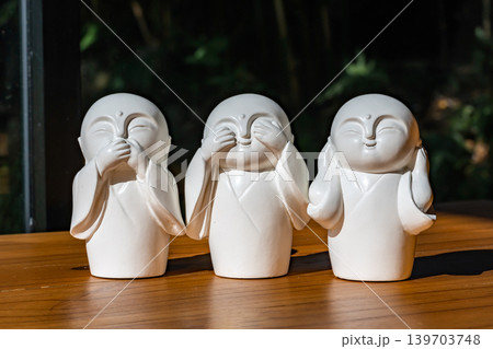 Three white monk figurines inspired by the Three Wise Monkeys philosophy are displayed as minimal zen decoration on a wooden tabletop with peaceful spiritual atmosphere. Three white monk figurines inspired by the Three Wise Monkeys philosophy are displayed as minimal zen decoration on a wooden tabletop with peaceful spiritual atmosphere. 139703748