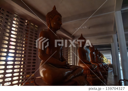 Row of large seated Buddha statues inside dimly lit Buddhist temple corridor. Spiritual atmosphere reflecting peace, meditation, devotion, and traditional Asian religious architecture. Row of large seated Buddha statues inside dimly lit Buddhist temple corridor. Spiritual atmosphere reflecting peace, meditation, devotion, and traditional Asian religious architecture. 139704327