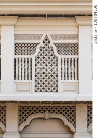 Elegant white Thai architectural facade featuring symmetrical lattice patterns and traditional ornamental details in minimalist temple design style. Elegant white Thai architectural facade featuring symmetrical lattice patterns and traditional ornamental details in minimalist temple design style. 139704336