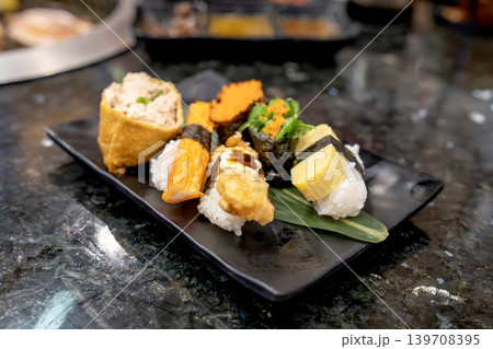 Assorted Japanese sushi platter featuring tamago, crab stick, inari tofu, and seaweed salad on a black plate. Elegant restaurant setting on dark marble tabletop with shallow depth of field. Assorted Japanese sushi platter featuring tamago, crab stick, inari tofu, and seaweed salad on a black plate. Elegant restaurant setting on dark marble tabletop with shallow depth of field. 139708395
