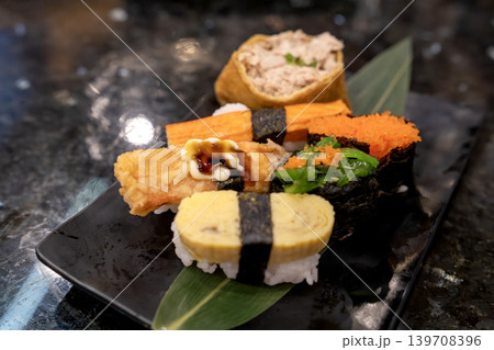 Assorted Japanese sushi platter with tamago nigiri, kani, tobiko gunkan, and seaweed salad on a black plate. Fresh seafood and rice served for a gourmet dining experience in a restaurant setting. 139708396