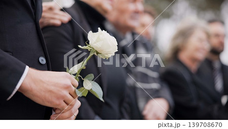 Hands, rose and a person at a funeral in a cemetery in grief while mourning loss at a memorial service. Death, flower and an adult in a suit at a graveyard in a crowd for an outdoor burial closeup Hands, rose and a person at a funeral in a cemetery in grief while mourning loss at a memorial service. Death, flower and an adult in a suit at a graveyard in a crowd for an outdoor burial closeup 139708670