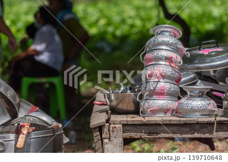 Traditional silver bowls kitchen utensils arranged on rustic wooden table during outdoor community gathering 139710648