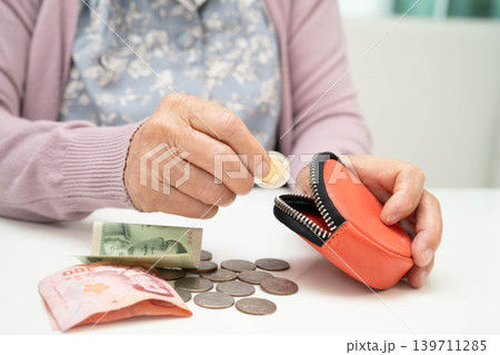 Asian senior or elderly old lady woman holding counting coin money in bag. Poverty, saving problem in retirement. Asian senior or elderly old lady woman holding counting coin money in bag. Poverty, saving problem in retirement. 139711285