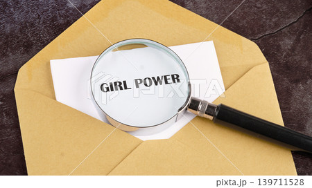 A magnifying glass rests on white paper displaying the phrase Girl Power, tucked inside a brown envelope on a dark surface. This highlights themes of womens strength and advocacy A magnifying glass rests on white paper displaying the phrase Girl Power, tucked inside a brown envelope on a dark surface. This highlights themes of womens strength and advocacy 139711528