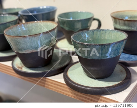 Ceramic cups with saucers displayed on shelf in pottery store, showcasing handcrafted design 139711900