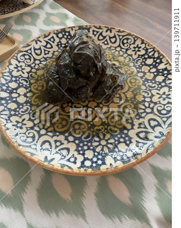 Stuffed grape leaves on ornate plate displayed on patterned tablecloth, suitable for backgrounds Stuffed grape leaves on ornate plate displayed on patterned tablecloth, suitable for backgrounds 139711911