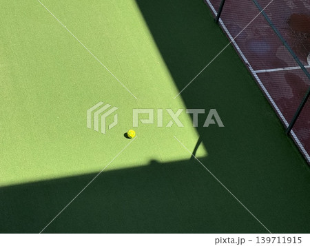 Yellow ball on green sports field with netted fence and sunlight shadow background 139711915