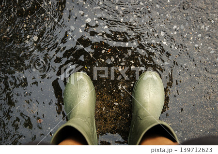 POV shot of person with rain boots standing on wet ground during rainfall, with raindrops in Rainy season POV shot of person with rain boots standing on wet ground during rainfall, with raindrops in Rainy season 139712623