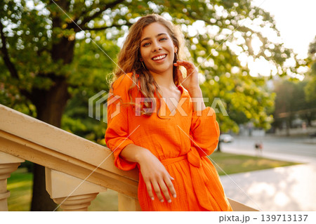 Young woman posing against backdrop of urban landscape in bright orange dress. Concept of lifestyle. 139713137