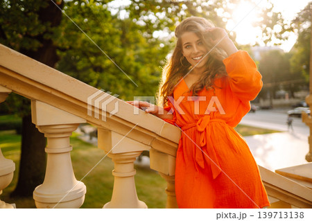 Young woman posing against backdrop of urban landscape in bright orange dress. Concept of lifestyle. 139713138