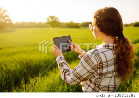 Young woman agronomist works on a modern digital tablet on a green wheat field. Young woman agronomist works on a modern digital tablet on a green wheat field. 139713298