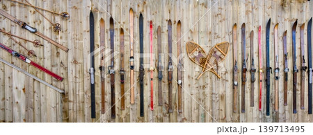 A collection of antique wooden skis and traditional leather-covered snowshoes hangs vertically A collection of antique wooden skis and traditional leather-covered snowshoes hangs vertically 139713495