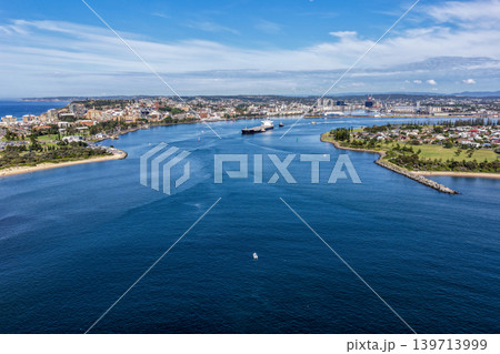 Aerial drone view of a large cargo ship being escorted by tug boats through Newcastle Harbour in New South Wales, Australia. Aerial drone view of a large cargo ship being escorted by tug boats through Newcastle Harbour in New South Wales, Australia. 139713999