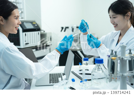 Asian women researchers analyzing cell culture in petri dish near laboratory bottle at workplace. Asian women researchers analyzing cell culture in petri dish near laboratory bottle at workplace. 139714241