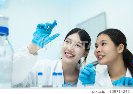 Asian women researchers analyzing cell culture in petri dish near laboratory bottle at workplace. Asian women researchers analyzing cell culture in petri dish near laboratory bottle at workplace. 139714246