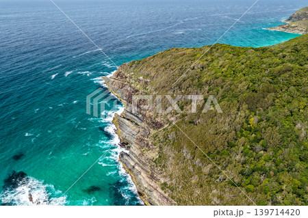 Rocky coastline at Cape Hawk in Forster featuring rugged coastal formations, ocean water and natural landscape. The scene highlights dramatic shoreline geology and scenic coastal environment. 139714420