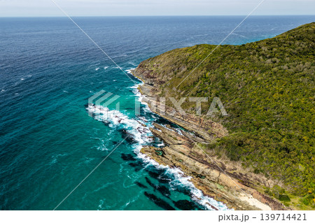 Rocky coastline at Cape Hawk in Forster featuring rugged coastal formations, ocean water and natural landscape. The scene highlights dramatic shoreline geology and scenic coastal environment. 139714421