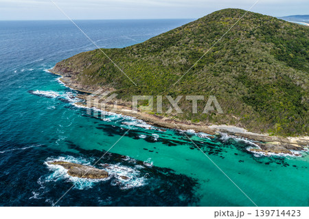 Rocky coastline at Cape Hawke in Forster featuring rugged coastal formations, ocean water and natural landscape. The scene highlights dramatic shoreline geology and scenic coastal environment. Rocky coastline at Cape Hawke in Forster featuring rugged coastal formations, ocean water and natural landscape. The scene highlights dramatic shoreline geology and scenic coastal environment. 139714423