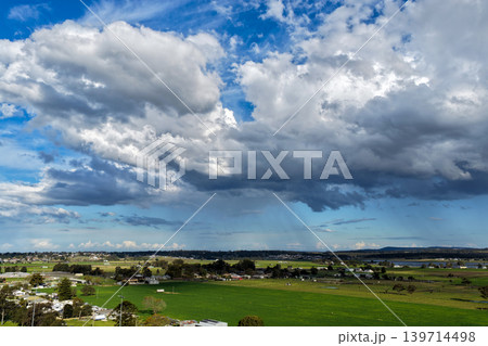 Aerial drone view of rural farmland in Maitland, New South Wales, Australia showing agricultural fields beneath cloudy blue sky. Scenic countryside landscape featuring farming land patterns in the Aerial drone view of rural farmland in Maitland, New South Wales, Australia showing agricultural fields beneath cloudy blue sky. Scenic countryside landscape featuring farming land patterns in the 139714498