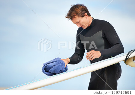 Surfer, man and getting ready with surfboard on beach with wetsuit, blue sky and cleaning with mock up space. Extreme sports, athlete and person by ocean for training, surfing workout and towel Surfer, man and getting ready with surfboard on beach with wetsuit, blue sky and cleaning with mock up space. Extreme sports, athlete and person by ocean for training, surfing workout and towel 139715691