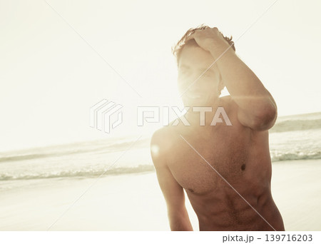 Man, shirtless and relaxing on beach at sunset, confidence and tourist at sea on summer holiday. Male person, lens flare and outdoor adventure for fun, calm ocean and peaceful environment in nature 139716203