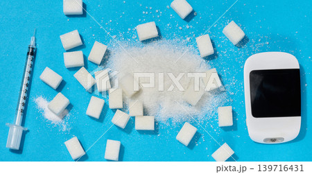 A glucometer, insulin syringe, and sugar cubes on a blue background, a concept for blood sugar control and diabetes treatment. A glucometer, insulin syringe, and sugar cubes on a blue background, a concept for blood sugar control and diabetes treatment. 139716431