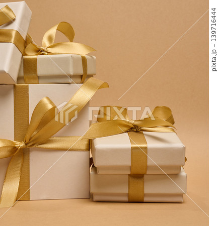 A stack of cream-colored gift boxes tied with gold satin ribbons and bows 139716444