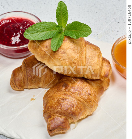 Three fresh golden croissants on a white board with fruit jam and mint Three fresh golden croissants on a white board with fruit jam and mint 139716459