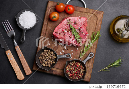 Fresh piece of raw beef on a wooden board with rosemary, cherry tomatoes, pepper and salt prepared for grilling steak 139716472