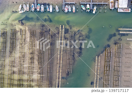 Aerial view of an oyster lease in the clear shallow waters of Wallis Lake in Forster NSW Australia. Drone photograph captures oyster farming infrastructure, transparent waterways and natural estuary Aerial view of an oyster lease in the clear shallow waters of Wallis Lake in Forster NSW Australia. Drone photograph captures oyster farming infrastructure, transparent waterways and natural estuary 139717117