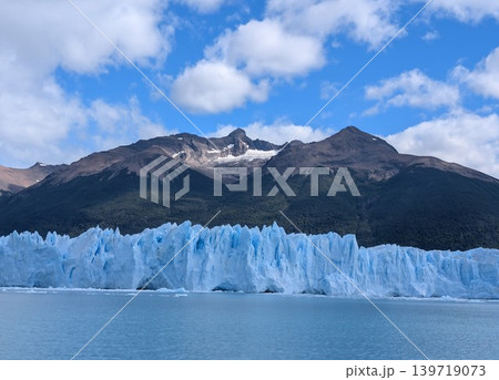 Blue ice wall of Perito Moreno Glacier against dark mountain peaks and blue sky 139719073