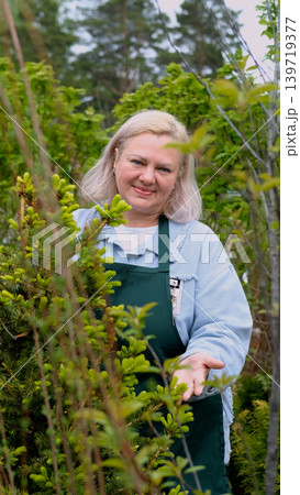 Portrait of happy female gardener standing among bright greenery of her garden Portrait of happy female gardener standing among bright greenery of her garden 139719377
