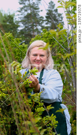 Portrait of happy female gardener standing among bright greenery of her garden 139719378