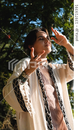 A beautiful brunette dressed in boho style meditates and dances in the forest. A magical ritual takes place against a green forest backdrop. 139719391